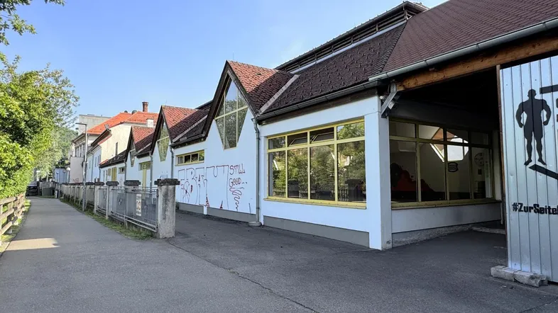 Gebäudeansicht mit mehreren Giebeldächern, großen Fenstern und einer Zufahrt zum Grundstück.
