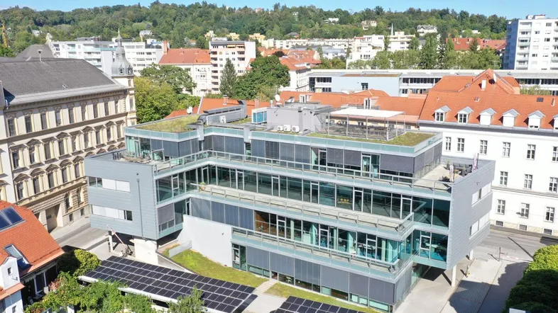 Luftaufnahme eines modernen Bürogebäudes mit Flachdach, Solaranlagen und begrüntem Dach in städtischer Umgebung.