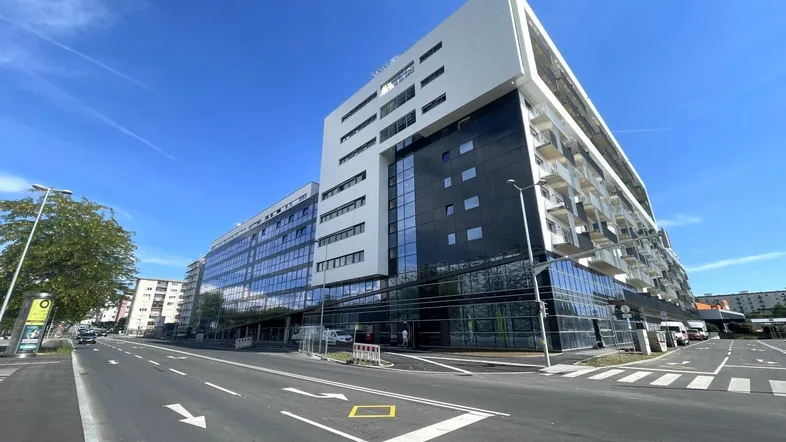 Modernes Geschäfts- und Wohngebäude mit Glasfassade und Balkonen an einer belebten Straße.