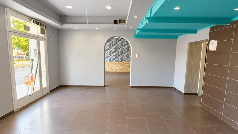Geräumiger Ladenbereich mit Fliesenboden, großen Fenstern und einer auffälligen türkisfarbenen Decke.