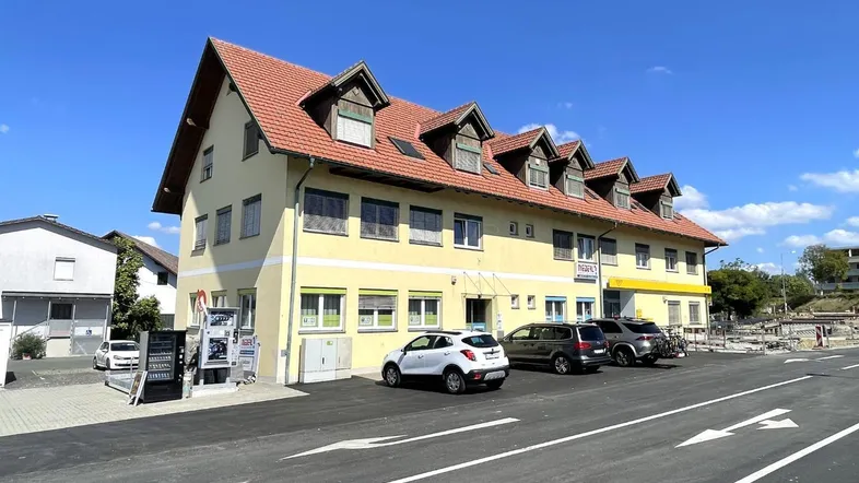 Gelbes Gebäude mit rotem Ziegeldach und mehreren Gauben, umgeben von einem Parkplatz.