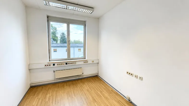 Heller, leerer Raum mit Holzfußboden und großem Fenster, ideal als Büro oder Arbeitszimmer.