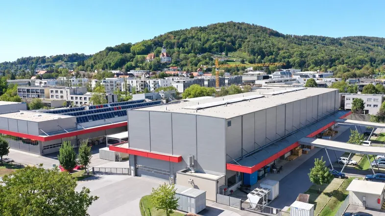 Luftaufnahme eines großen Industrie- und Lagerkomplexes mit umliegenden Parkplätzen und grüner Umgebung.