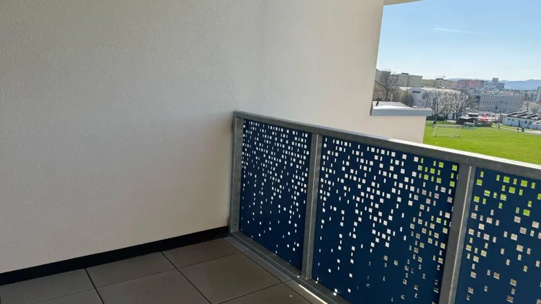 Moderner Balkon mit Fliesenboden und perforiertem Geländer, bietet einen weiten Blick ins Grüne.