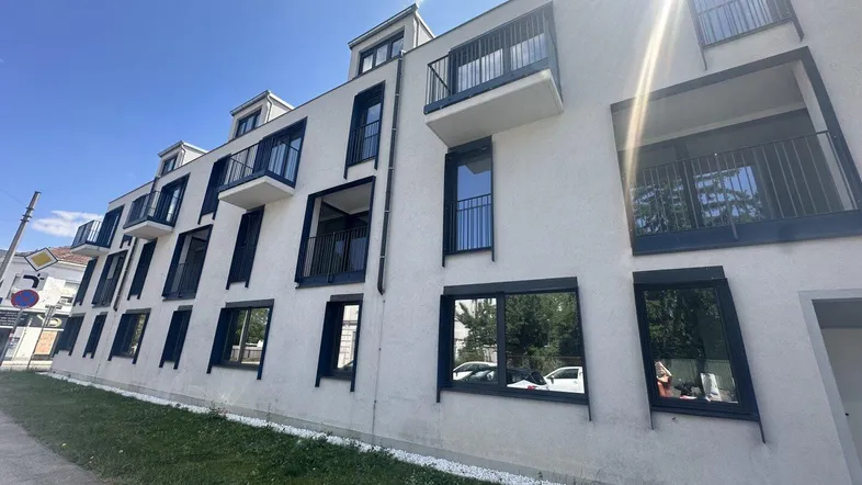 Moderne Wohnhausfassade mit Balkonen und großen Fenstern unter blauem Himmel.