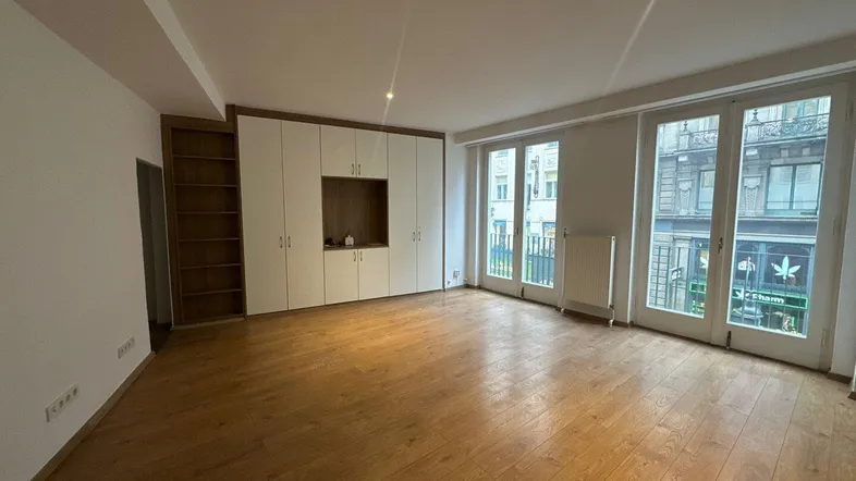 Geräumiges Zimmer mit Holzboden, Einbauschränken und großen Fenstern zur Straße.