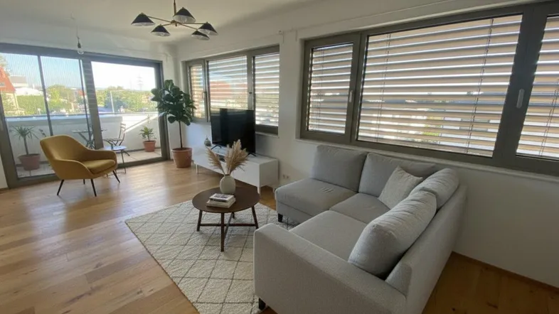 Helles Wohnzimmer mit Holzboden, modernem Sofa und Zugang zu einem Balkon.