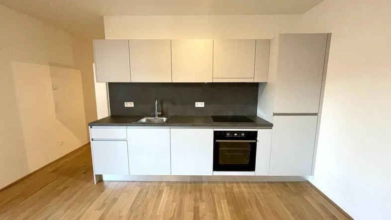 Moderne Einbauküche mit hellen Fronten und Holzboden in einem leeren Raum, bereit zur Nutzung.