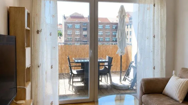 Helles Wohnzimmer mit Holzboden, bequemer Couch und Zugang zu einem möblierten Balkon.