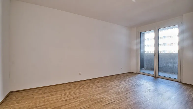 Helles, leeres Zimmer mit Parkettboden und Zugang zu einem Balkon, ideal als Wohnbereich.