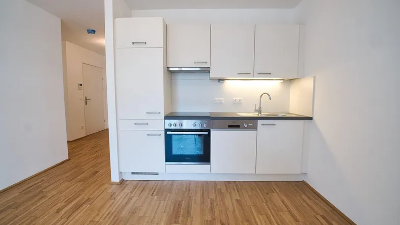 Moderne Einbauküche mit weißen Schränken, integrierten Geräten und Parkettboden in einem hellen Raum.