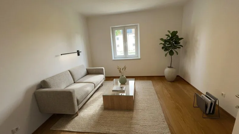 Helles Wohnzimmer mit Holzboden, einem bequemen Sofa und einem Fenster mit Blick nach draußen.