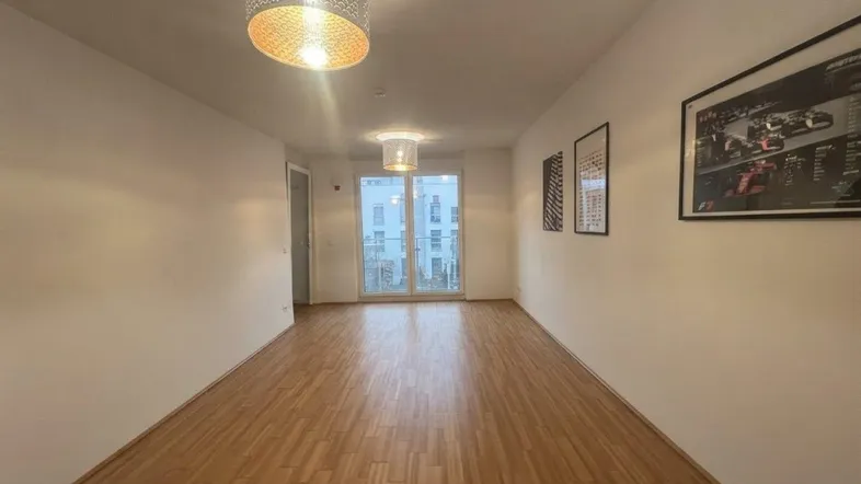 Langer Flur mit hellem Parkettboden und Zugang zu einem Balkon, der viel Tageslicht hereinlässt.