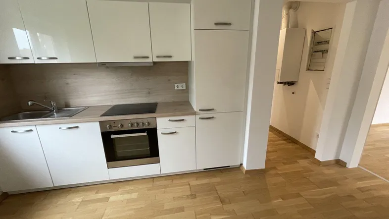 Moderne Einbauküche mit weißen Hochglanzfronten, integrierten Geräten und hellem Parkettboden.