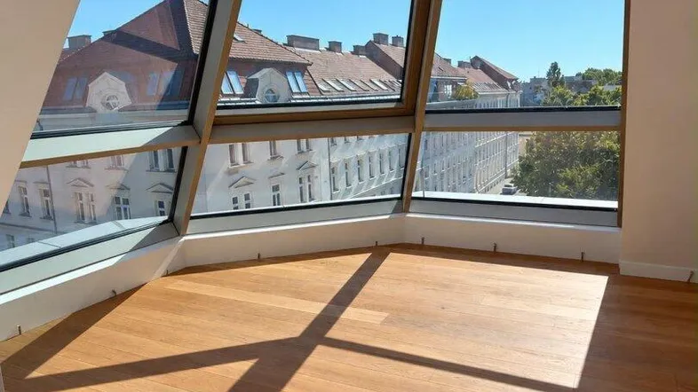 Heller Raum mit großen, schrägen Fenstern und Blick auf die Stadt.