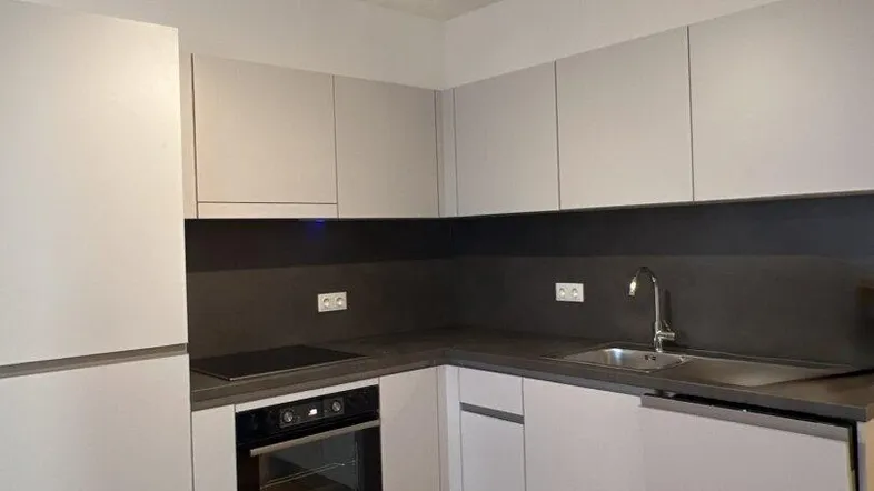 Moderne Einbauküche mit hellgrauen Fronten, dunkler Arbeitsplatte und integrierten Geräten.