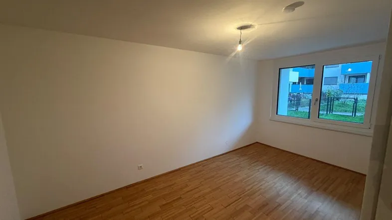 Helles, leeres Zimmer mit Parkettboden und Blick ins Grüne, bereit zur individuellen Gestaltung.