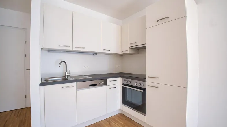 Moderne Einbauküche mit weißen Schränken, dunkler Arbeitsplatte und Holzboden.