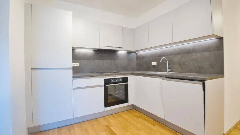 Moderne Einbauküche mit hellgrauen Fronten, dunkler Arbeitsplatte und Holzboden.
