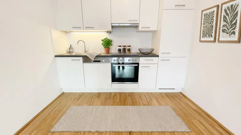 Moderne Küche mit weißen Schränken, dunkler Arbeitsplatte und integrierten Geräten, ergänzt durch einen Teppich auf dem Parkettboden.