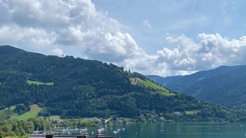 Panoramablick auf den See und die umliegenden Berge unter einem bewölkten Himmel.