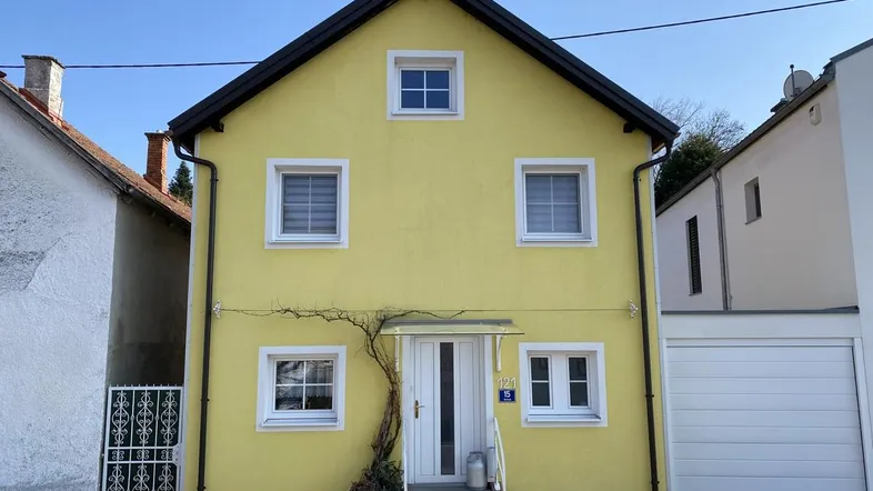 Gelbes Einfamilienhaus mit weißem Eingangsbereich und angrenzender Garage unter blauem Himmel.