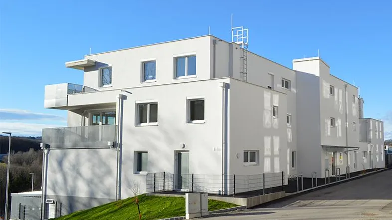 Modernes Mehrfamilienhaus mit weißer Fassade und Balkonen in grüner Umgebung.