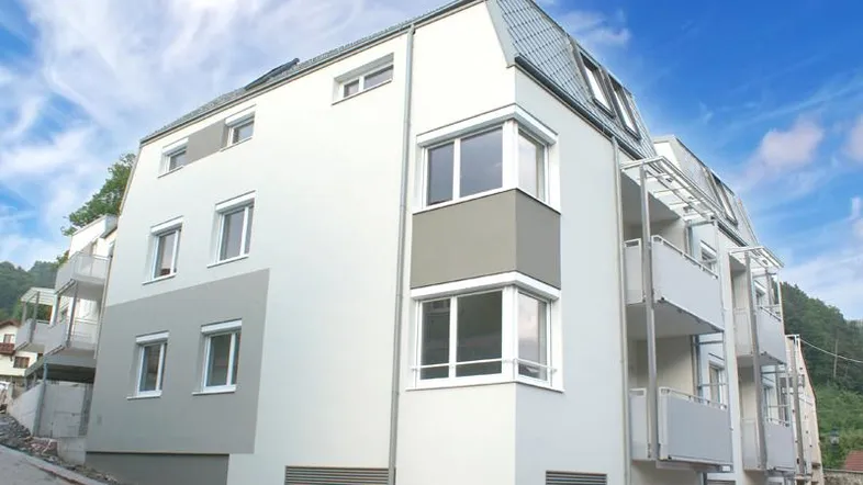 Modernes Mehrfamilienhaus mit weißer und grauer Fassade, Balkonen und großen Fenstern.