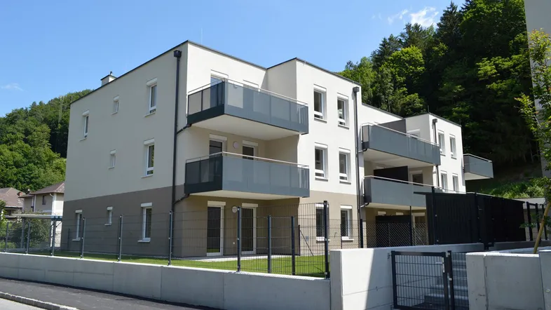 Modernes Mehrfamilienhaus mit Balkonen und kleinen Gärten, umgeben von grüner Natur.