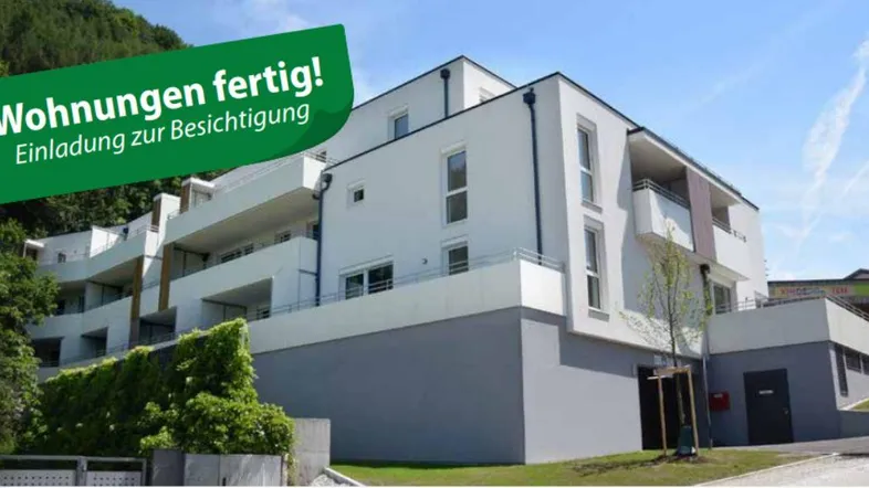 Modernes Mehrfamilienhaus mit weißer Fassade, Balkonen und grüner Umgebung am Hang.