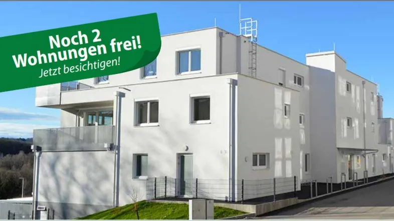 Modernes Neubau-Wohngebäude mit weißer Fassade und Balkonen, umgeben von grünen Hügeln.