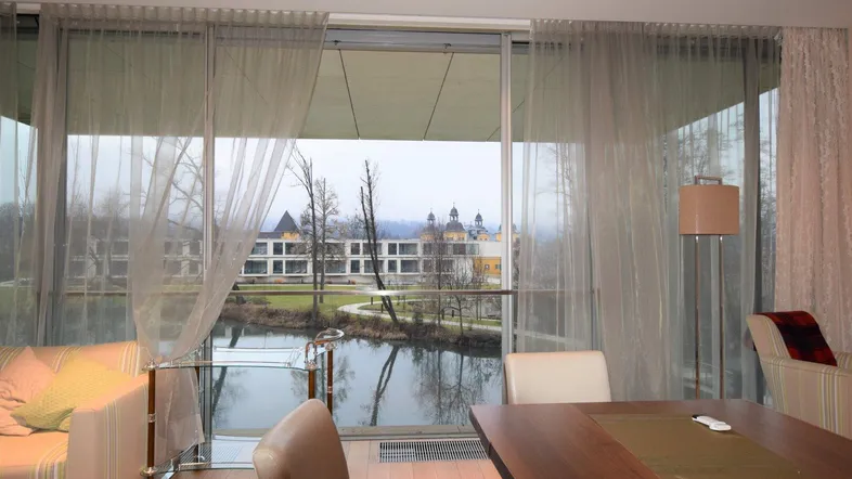 Helles Wohn- und Esszimmer mit großen Fenstern, die einen Blick auf den See und ein Schloss bieten.
