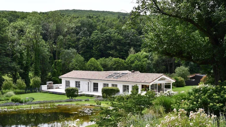 Weißes Landhaus mit Ziegeldach, umgeben von üppiger Natur und einem Teich.