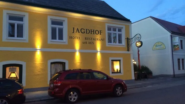 Gelbes Gebäude mit beleuchteter Fassade und parkenden Autos bei Dämmerung, gut beleuchtet.