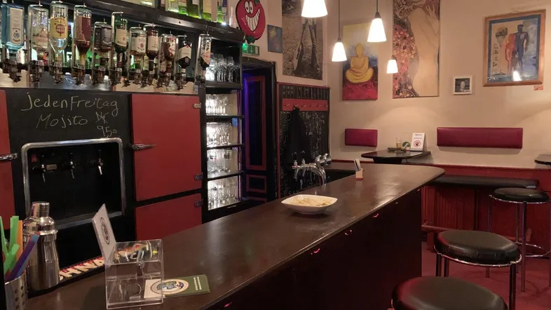 Gemütliche Bar mit dunklem Holztresen, Flaschenregalen und Hängelampen, bereit für Gäste.