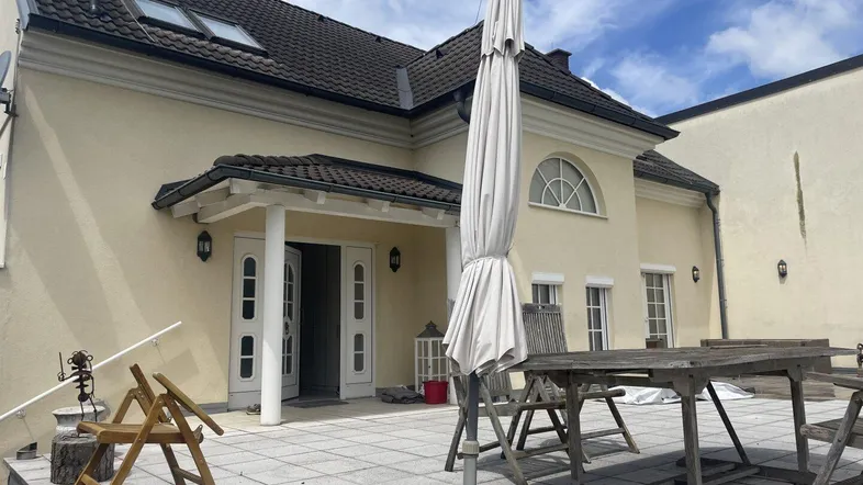 Große gepflasterte Terrasse mit Gartenmöbeln und Sonnenschirm vor dem Haus.