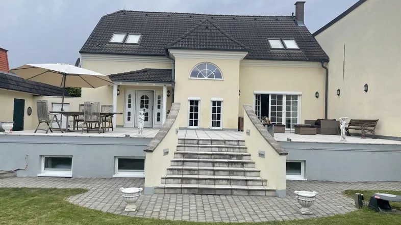 Großzügige Terrasse mit Sitzgelegenheiten und Treppe zum Garten, umgeben von einer gepflegten Rasenfläche.