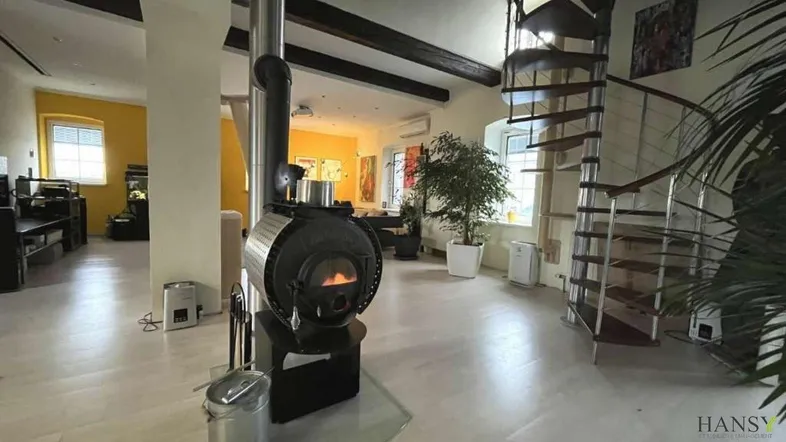 Geräumiges Wohnzimmer mit modernem Kaminofen, freiliegenden Holzbalken und Wendeltreppe.