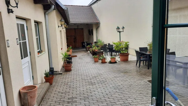 Gepflasterter Innenhof mit Pflanzen und Sitzgelegenheiten, umgeben von Gebäuden und einer gemütlichen Atmosphäre.