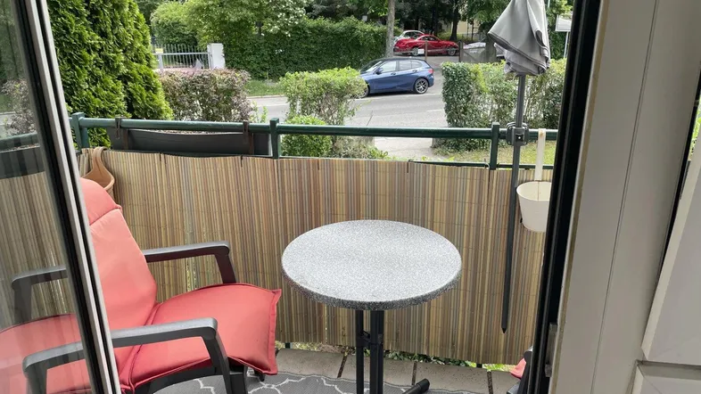 Kleiner Balkon mit Sitzgelegenheit und Blick auf die Straße und grüne Umgebung.