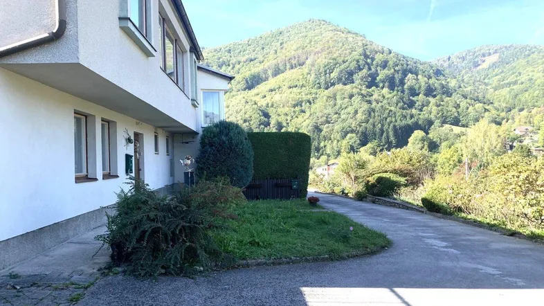 Seitenansicht des Hauses mit Zufahrt und Blick auf die umliegende grüne Hügellandschaft.