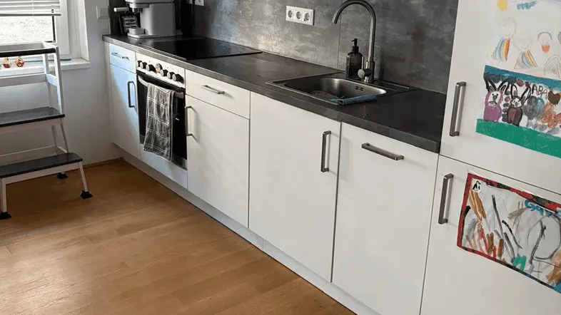 Moderne Küche mit weißen Schränken, dunkler Arbeitsplatte und hellem Holzfußboden.