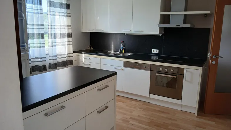 Moderne Küche mit weißen Schränken, dunkler Arbeitsplatte und hellem Laminatboden.