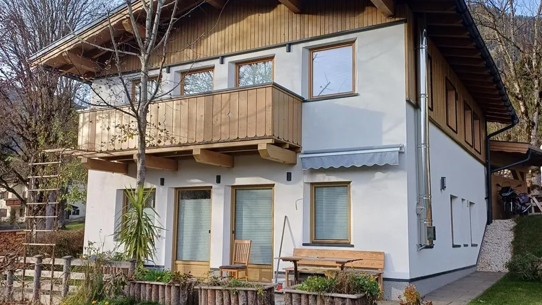 Charmantes Haus im alpinen Stil mit Holzbalkon und kleiner Terrasse im Vorgartenbereich.