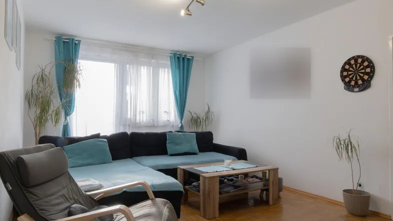 Gemütliches Wohnzimmer mit großem Ecksofa, Parkettboden und einem Fenster mit Vorhängen.