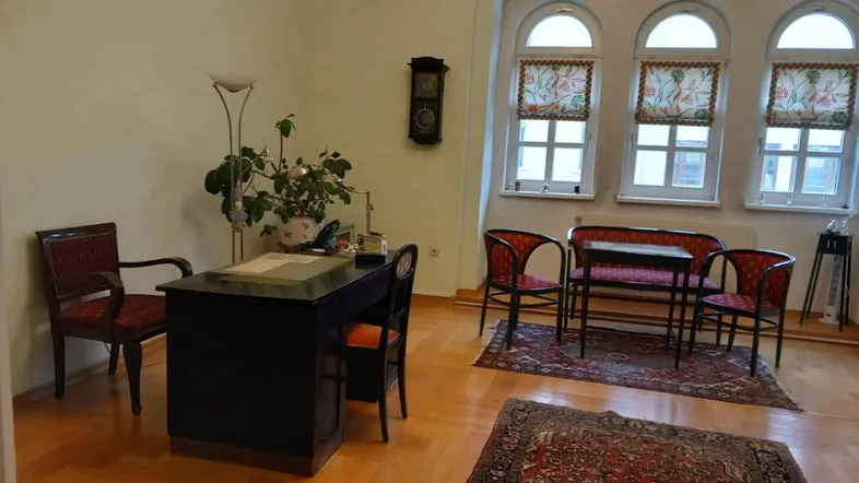 Klassisches Büro mit Holzboden, antiken Möbeln und Bogenfenstern, ausgestattet mit einem Schreibtisch und Sitzgelegenheiten.
