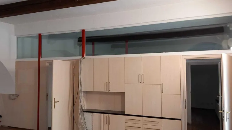 Ein Innenraum mit hellen Einbauschränken, sichtbaren Holzbalken und freiliegenden Kabeln, möglicherweise ein Büro.