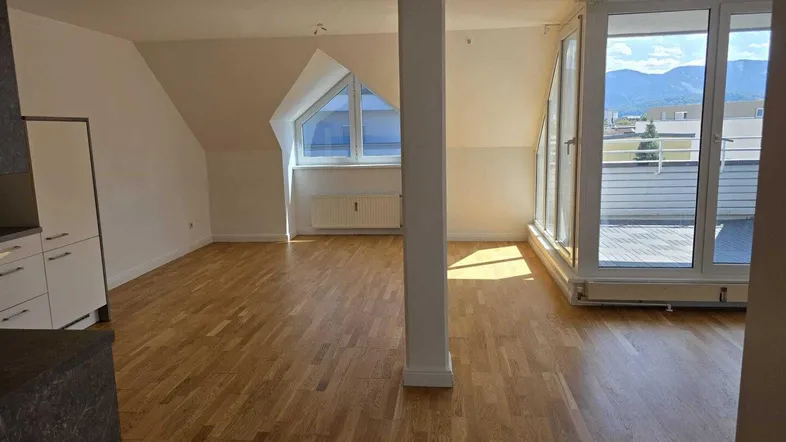 Heller Wohnbereich im Dachgeschoss mit Holzboden, Zugang zur Terrasse und Bergblick.