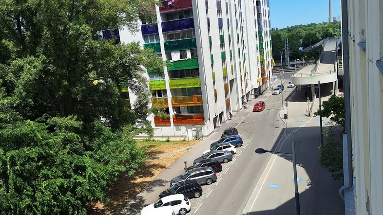 Moderne Wohngebäude mit farbigen Balkonen, einer Straße und Bäumen unter blauem Himmel.
