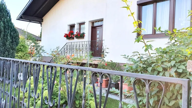 Vorderansicht des Hauses mit weißer Fassade, braunen Fenstern und einem gepflegten Vorgarten.